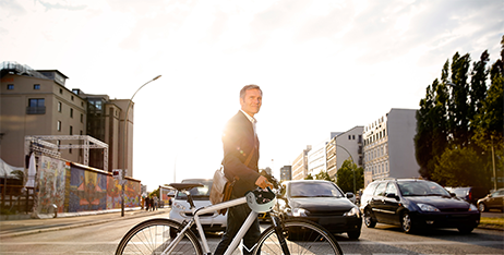 a man in a suit wheeling a bicycle across a wide city street