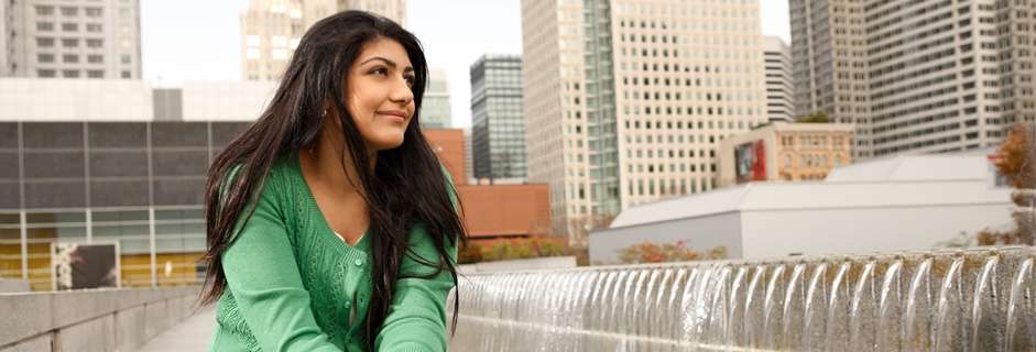 A woman sits outside an office by a fountain and looks at the sky